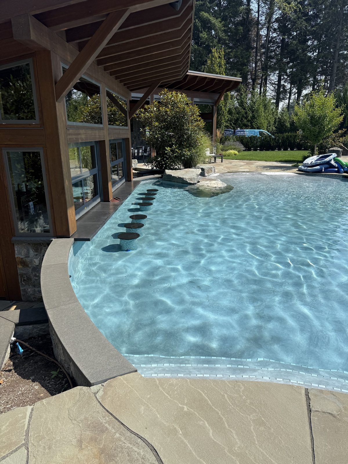 Freeform pool beside a cedar and stone home, with the JK service van on site